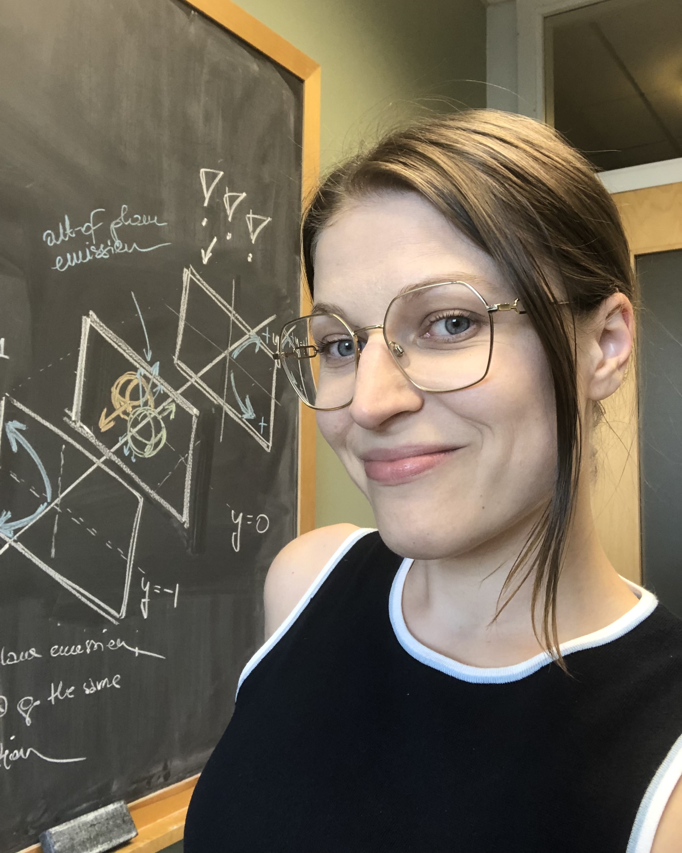 Photo of Agnieszka Sorensen in front of a blackboard showing sketches of
		    heavy-ion collisions.